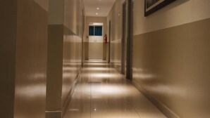 A hotel corridor with a tiled floor, recessed lighting, a fire extinguisher, and a framed picture on the wall. - Hotel Brickell (Lima)