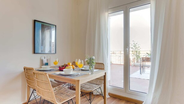 Ein Essbereich mit Tisch für zwei Personen, Korbstühle und Blick auf einen Balkon mit Gartenmöbeln.