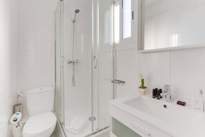 Une salle de bain moderne avec une douche en verre, des toilettes blanches et un lavabo équipé de produits de toilette.