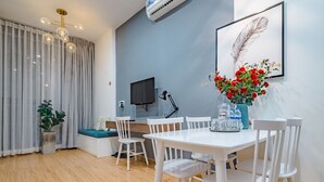 Ein modernes Wohnzimmer mit einem weißen Esstisch, weißen Stühlen, einem Fernseher, einer Pflanze und einem gerahmten Kunstwerk an der Wand.