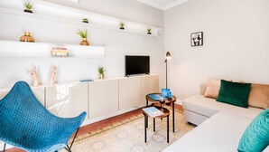 A modern living room with a sofa, a blue chair, a TV, and a bookshelf with plants. - Sweett | Rocafort 103 (Barcelona)