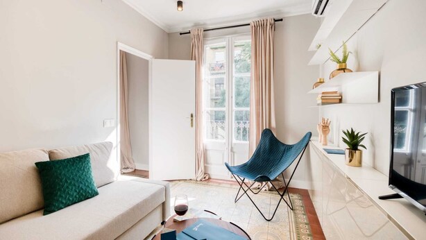 A modern living room with a sofa, a blue chair, a TV, and a window with curtains. - Sweett | Rocafort 103 (Barcelona)