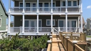 Un immeuble résidentiel de deux étages, doté d’un balcon à chaque étage, d’une terrasse en bois à l’avant et surplombant un ciel dégagé.