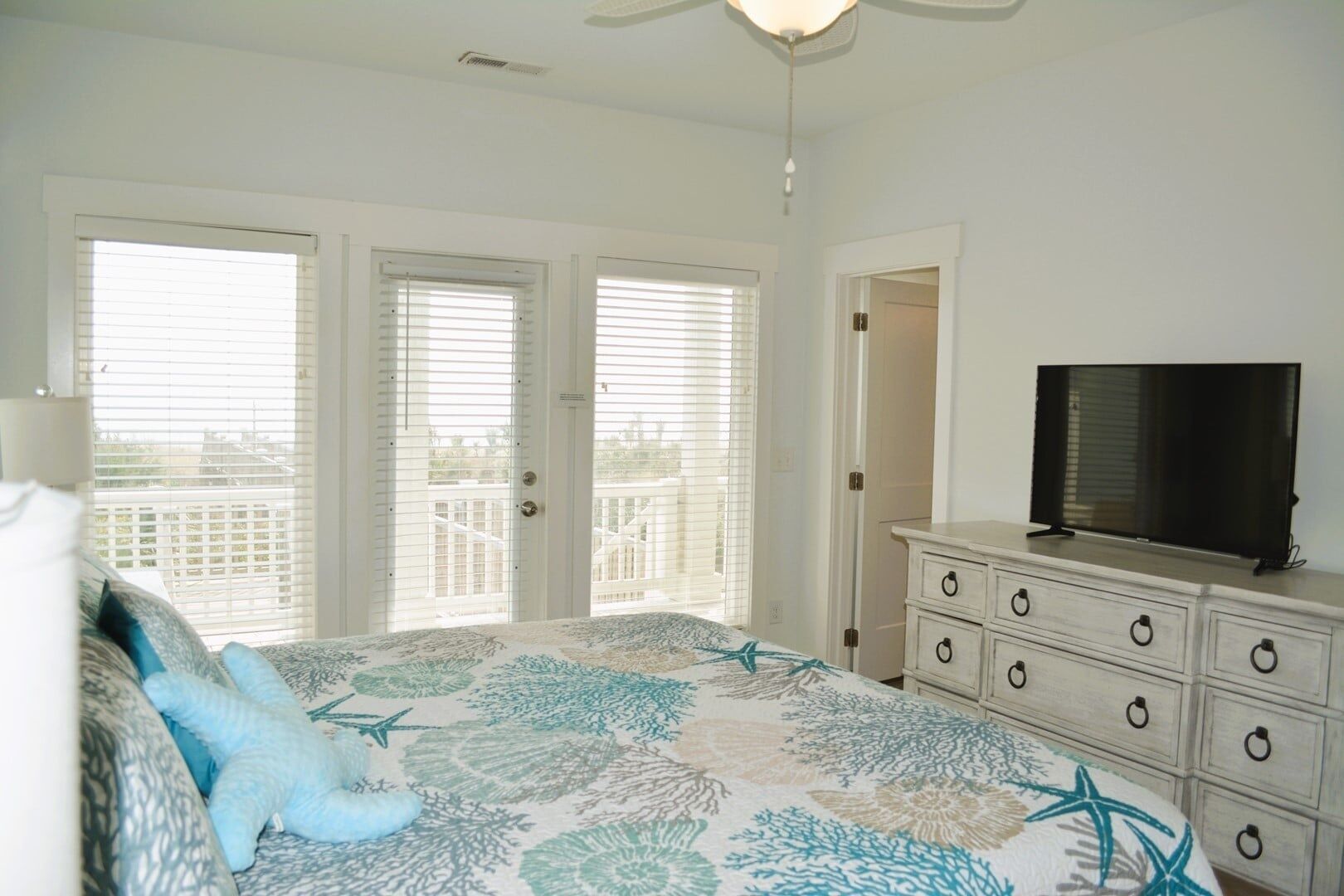 A bedroom with a bed, a dresser, a television, and a balcony with a railing.