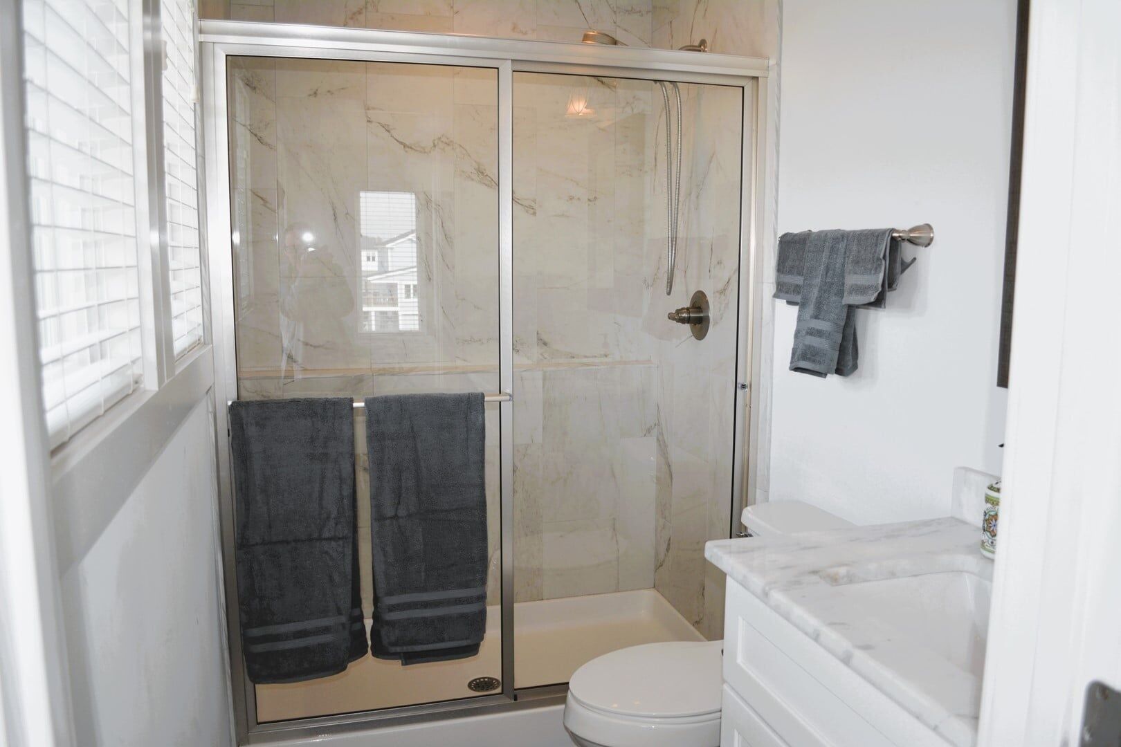 A bathroom with a glass-enclosed shower, a white toilet, and a marble sink.