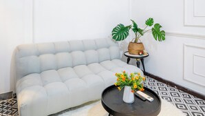 A modern living room with a light grey sofa, a round black coffee table with a vase of flowers, a hanging red light fixture, and a projector mounted on the ceiling.