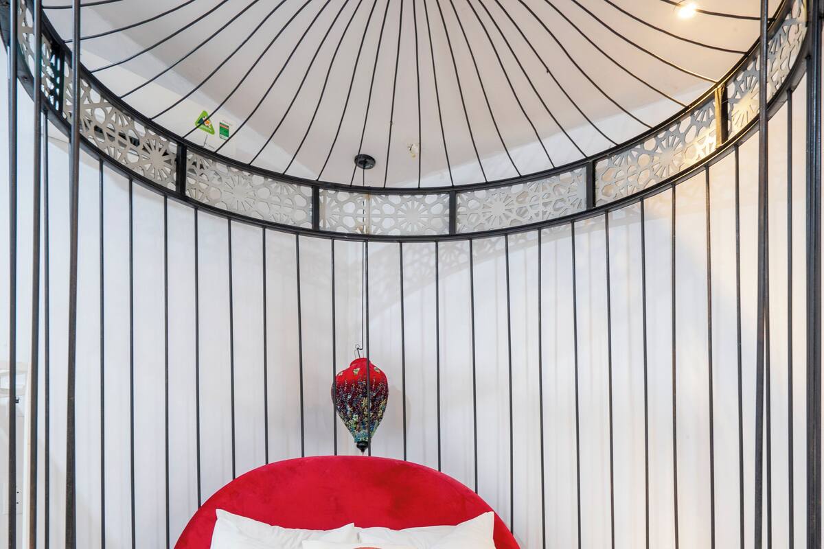 A circular bed with a red headboard, white bedding, and a patterned throw blanket.