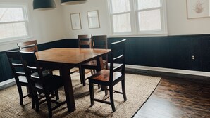 A dining room with a wooden table and chairs, black pendant lights, and large windows with white frames. - CritzerShop - route 151- walk to the Brewey! (Afton)