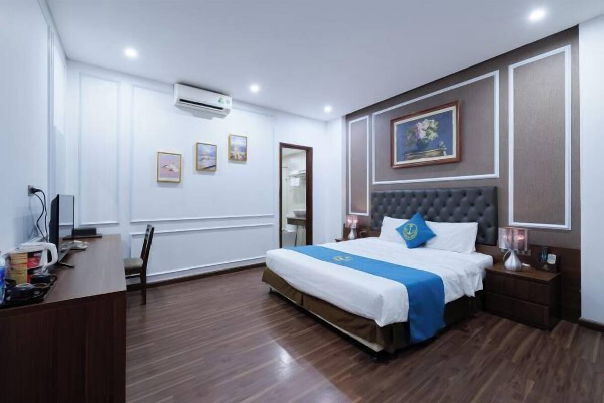 A hotel room with a bed, bedside tables, a desk, and an air conditioning unit.