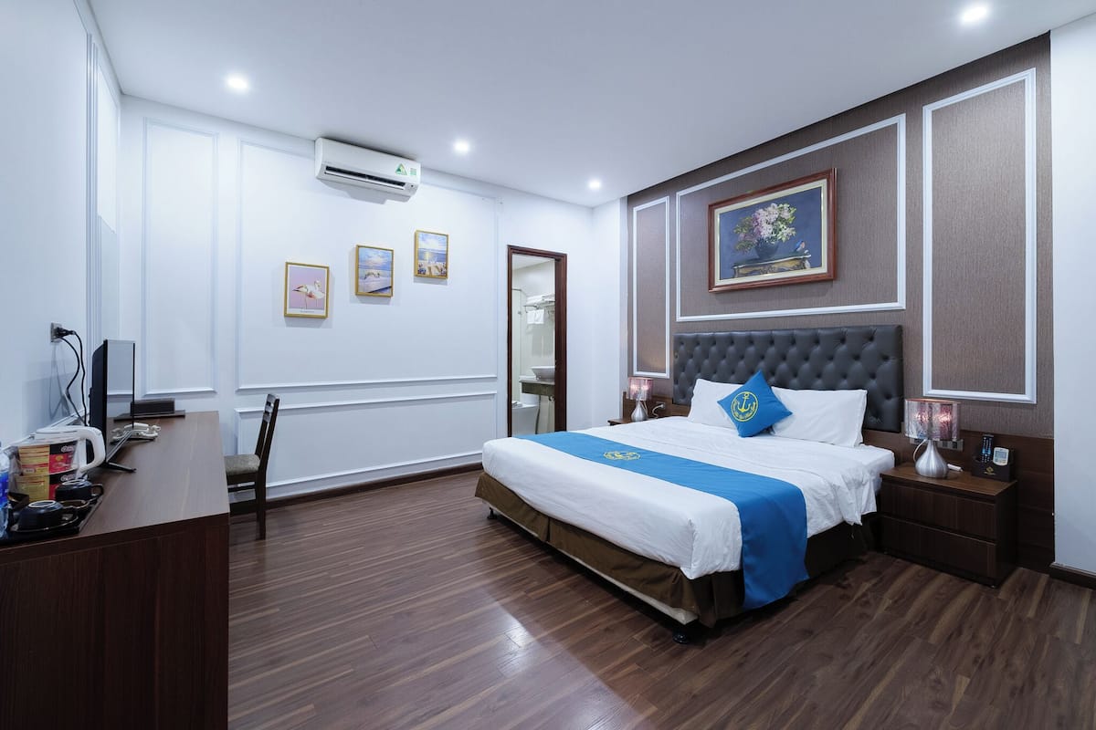 A hotel room with a bed, bedside tables, a desk with a chair, a wardrobe, and a mirror.