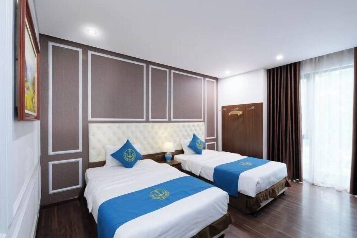 A hotel room with two beds, a headboard with a tufted design, a nightstand, and a window with curtains.