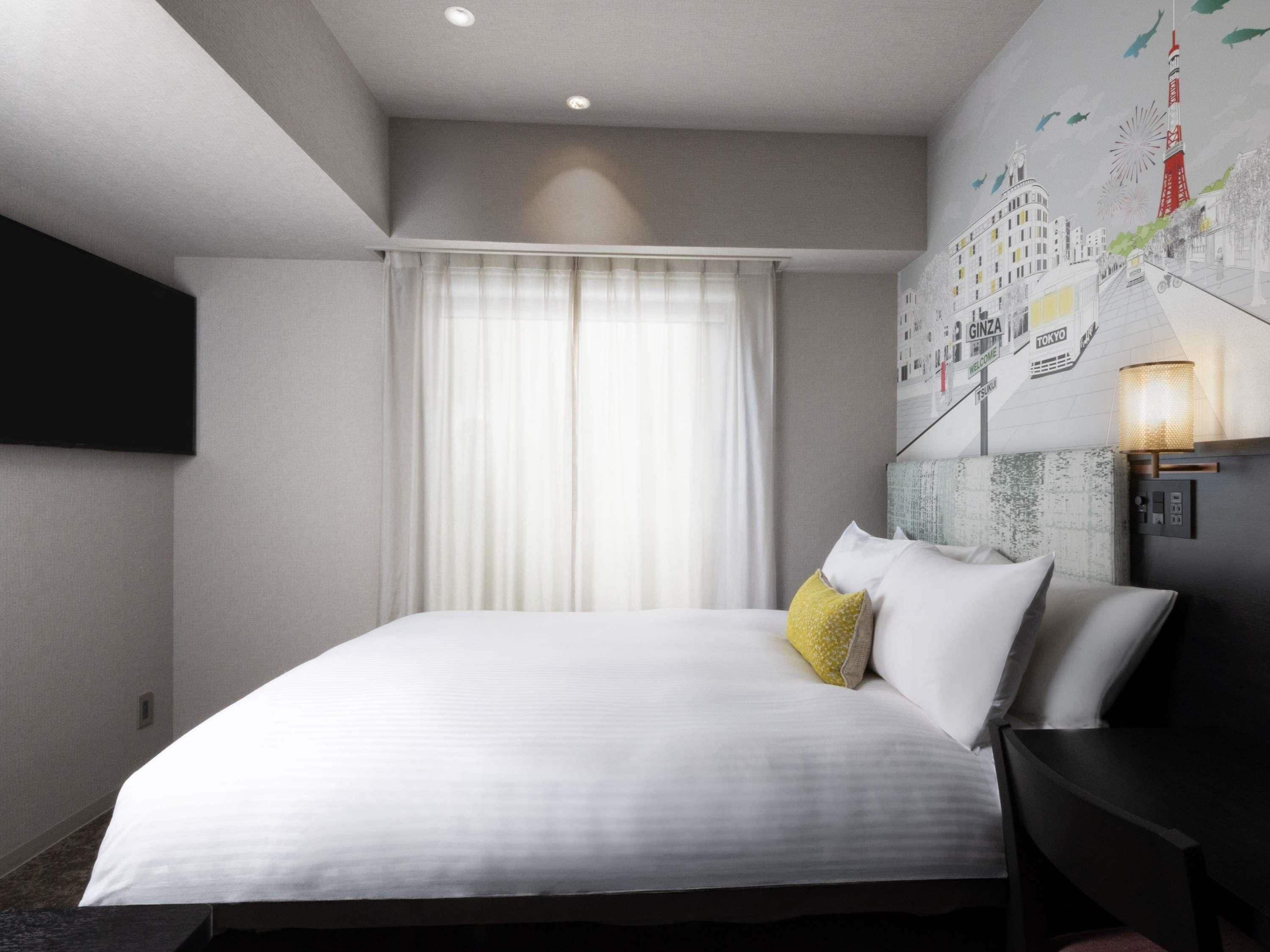 A hotel room with a large bed, a flat-screen TV mounted on the wall, a window with curtains, and a wall mural.