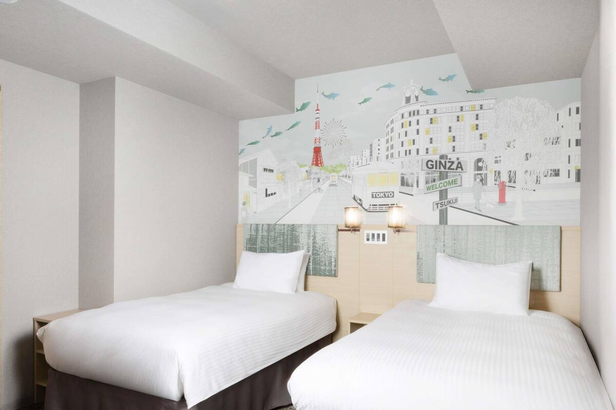 Une chambre d’hôtel avec deux lits, une fresque représentant un paysage urbain sur le mur et une table de chevet avec deux lampes.