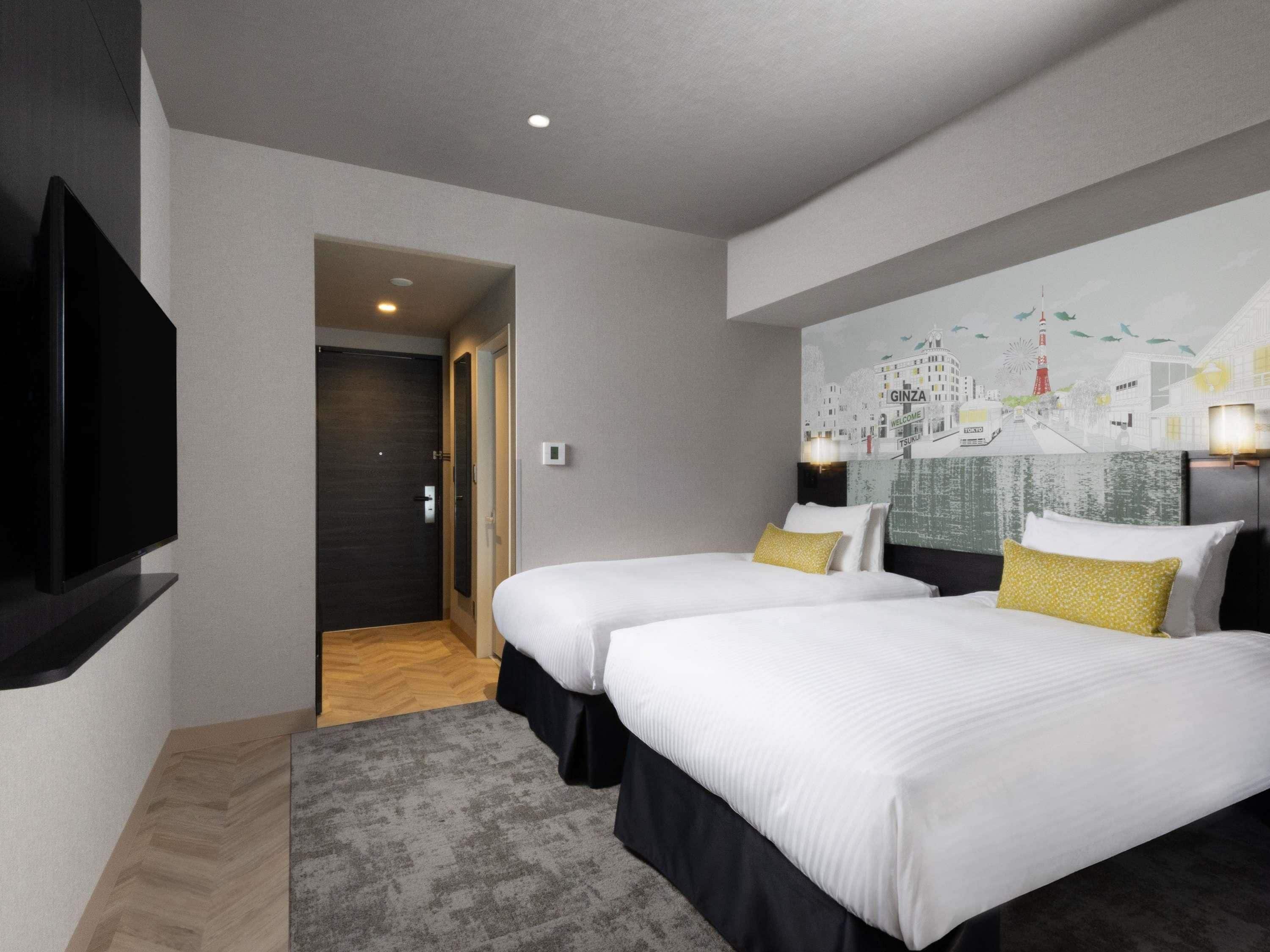 Habitación de hotel con dos camas, un televisor de pantalla plana, un mural con vista a la ciudad y piso de madera.