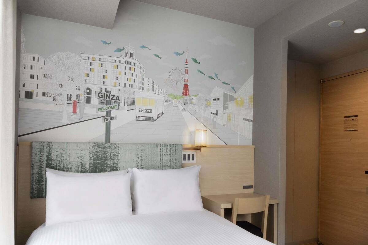 Une chambre d’hôtel avec un lit, une table de chevet, une lampe fixée au mur et une fresque représentant le quartier de Ginza à Tokyo.