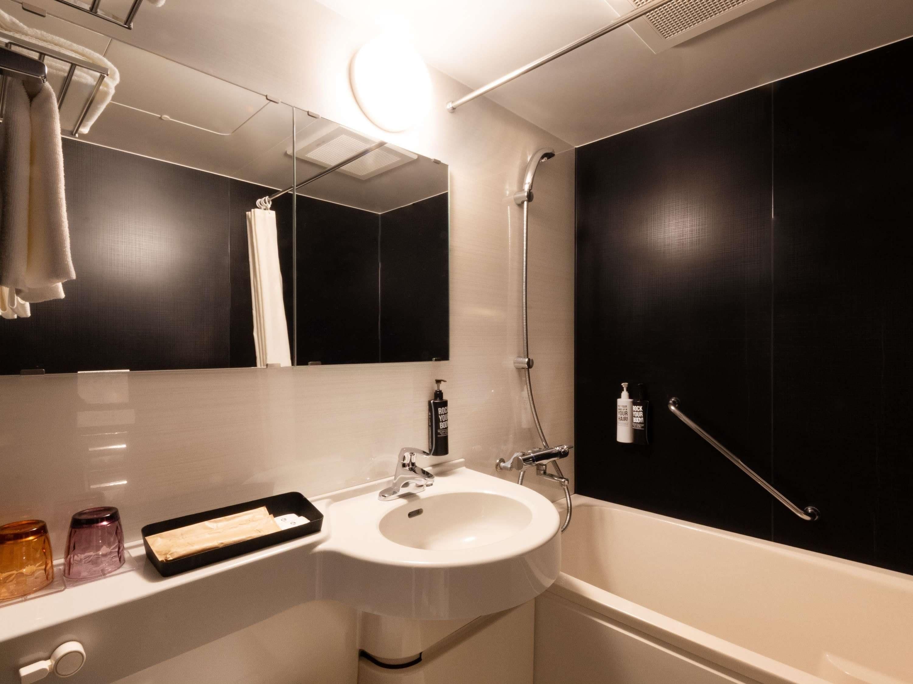 A modern bathroom with a white sink, a mirror, a handheld showerhead, and a towel rack.