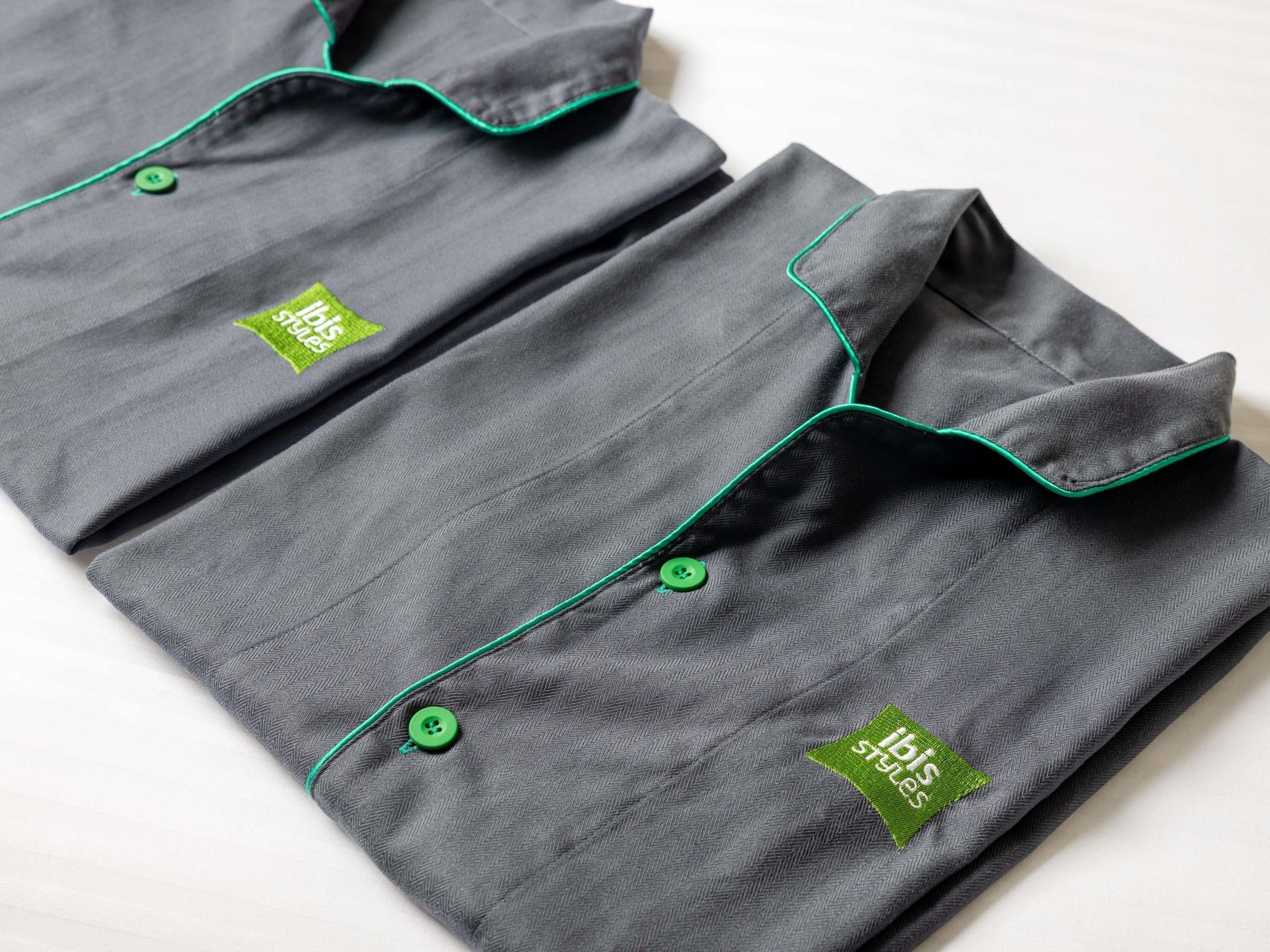 Een netjes gevouwen grijs kledingstuk met groene biezen en een klein logo op de zak.