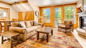 A cozy living room with a sofa, coffee table, and armchair, wooden beams on the ceiling, large windows, and a fireplace. - Spacious 1br -river Run Village-hot Tub & Kids Ski Free 1 Bedroom Condo by RedAwning (Keystone)
