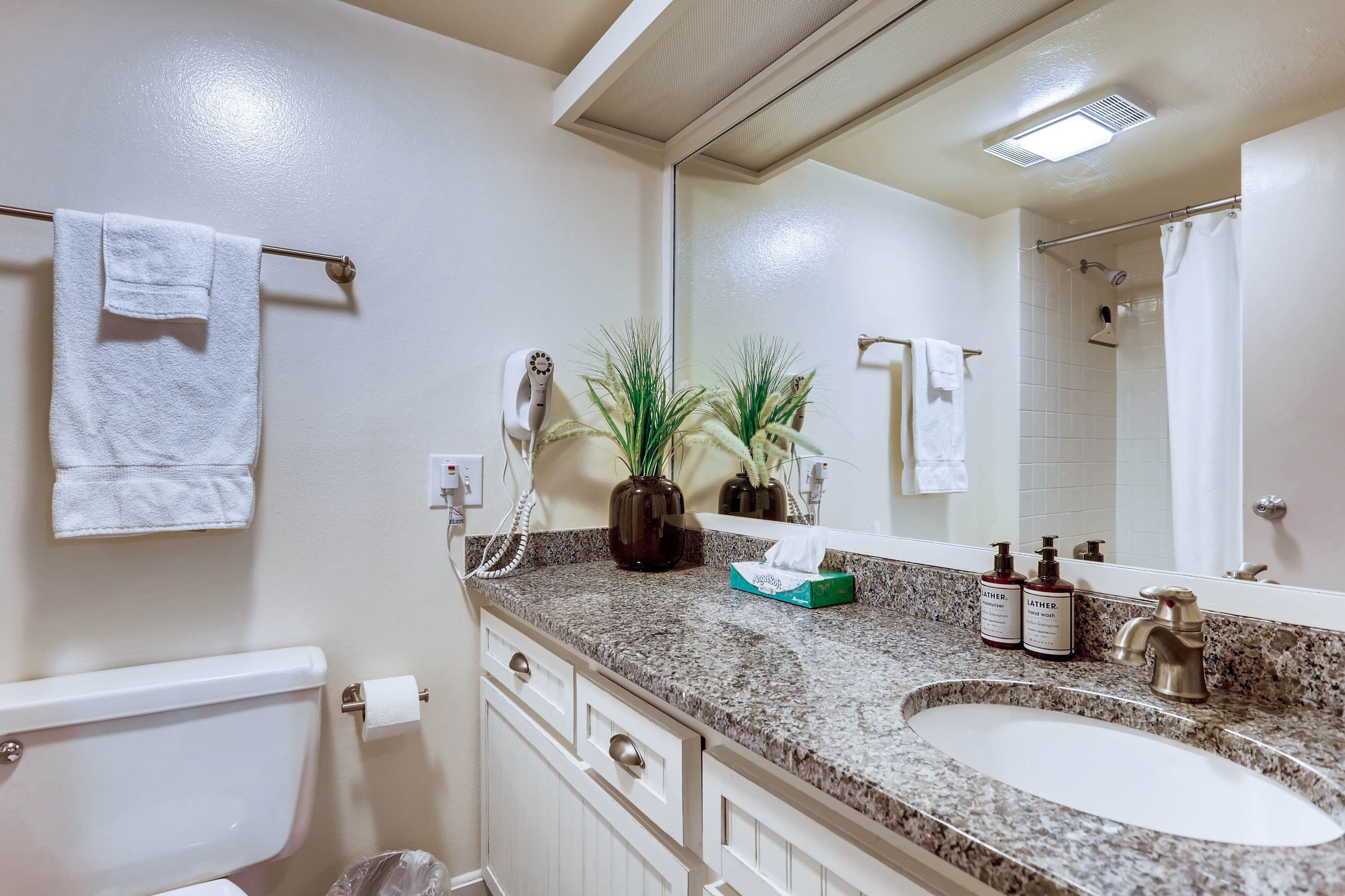 Un baño con inodoro blanco, lavabo con encimera de granito, espejo y perchero para toallas.