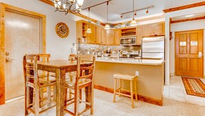 A kitchen with wooden cabinets, a central island, and a dining area with a wooden table and chairs. - Updated 1br Premier  At Black Bear Lodge- Kids Ski Free 1 Bedroom Condo by RedAwning (Keystone)