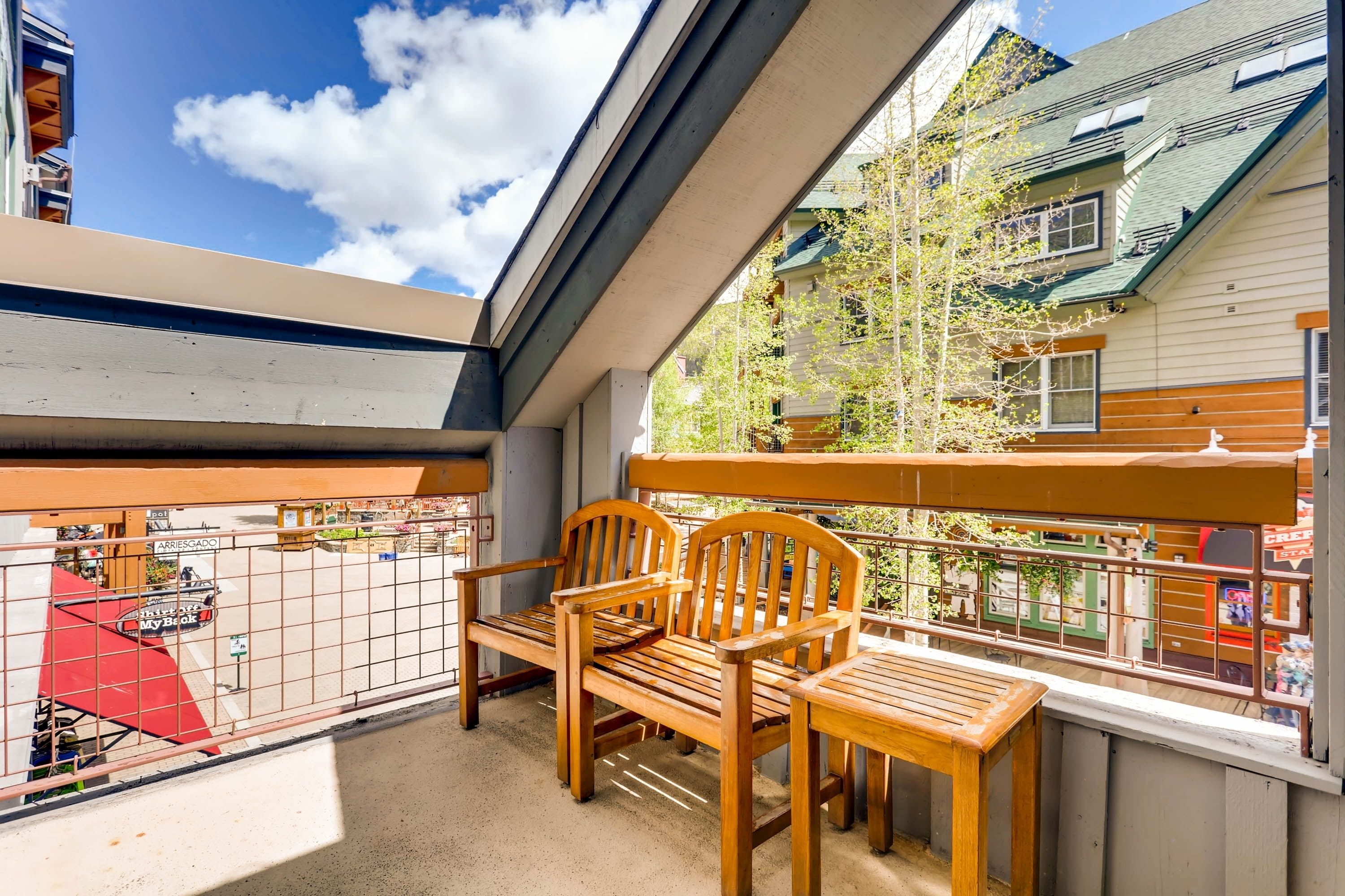 A balcony with wooden furniture, a view of the street, and neighboring buildings.