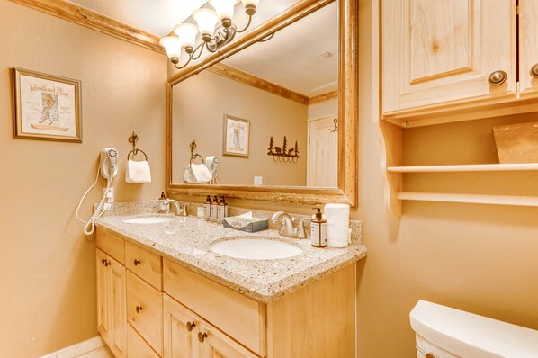 A bathroom with two sinks, a mirror, wooden cabinets, a towel rack, and a toilet.