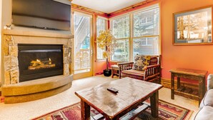 A cozy living room with a stone fireplace, a flat-screen TV, and a comfortable seating area with a patterned rug. - Updated 1br Premier  At Black Bear Lodge- Kids Ski Free 1 Bedroom Condo by RedAwning (Keystone)