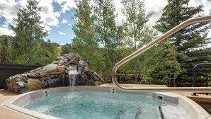 A hot tub with a waterfall feature, surrounded by a stone wall and set in a landscaped area with trees. - Updated 1br Premier  At Black Bear Lodge- Kids Ski Free 1 Bedroom Condo by RedAwning (Keystone)