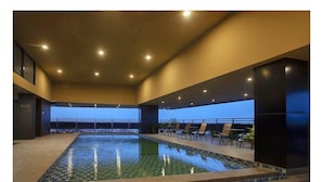 Une piscine intérieure avec vue sur l’océan, entourée de chaises longues et dotée d’un sol carrelé.