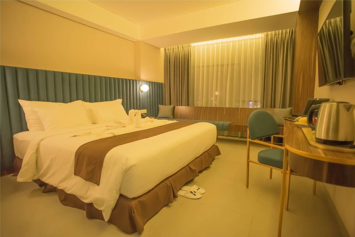 Une chambre d’hôtel avec un lit, un bureau, une chaise, une télévision et une fenêtre avec des rideaux.