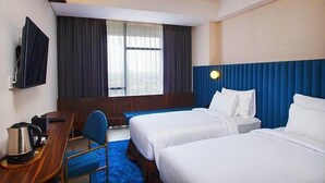 Une chambre d’hôtel avec deux lits, un bureau avec une chaise, une télévision et une fenêtre avec des rideaux.
