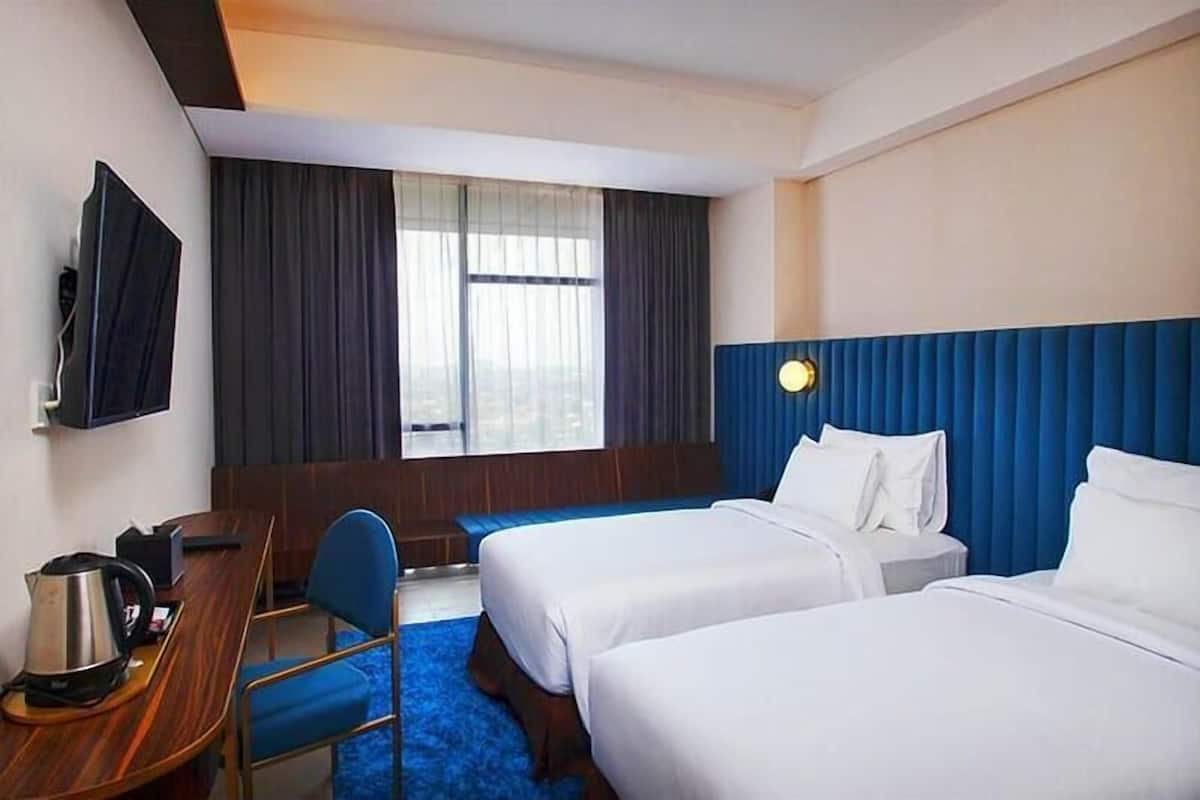 Une chambre d’hôtel avec deux lits, un bureau avec une chaise, une télévision et une fenêtre avec des rideaux.