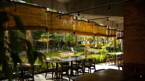 Un espacio de comedor al aire libre con mesas y sillas, rodeado de exuberante follaje y un estanque.