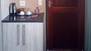 Une chambre avec une porte en bois, une kitchenette équipée d’une machine à café et un téléviseur fixé au-dessus du comptoir.