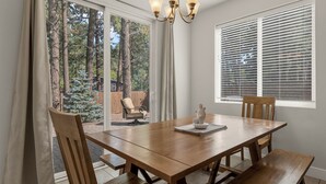 A dining area with a wooden table, four chairs, a chandelier, and a view of a forest through a sliding glass door. - Beautiful home! Central AC! 5 mins to Downtown! Great setting! 20% Monthly Disc! (Flagstaff)