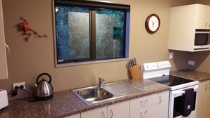 Una cocina con ventana, reloj, estufa y lavamanos.