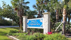 Señal de bienvenida a Longboat Key, rodeada de palmeras y plantas con flores.