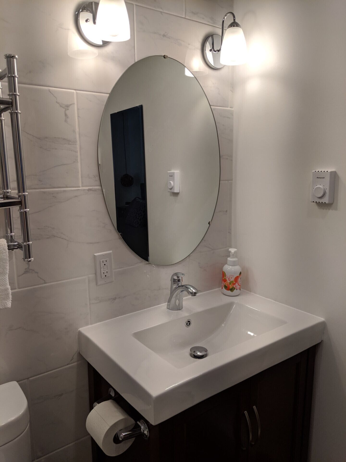 A bathroom with a white sink, a round mirror, and two wall-mounted lights.