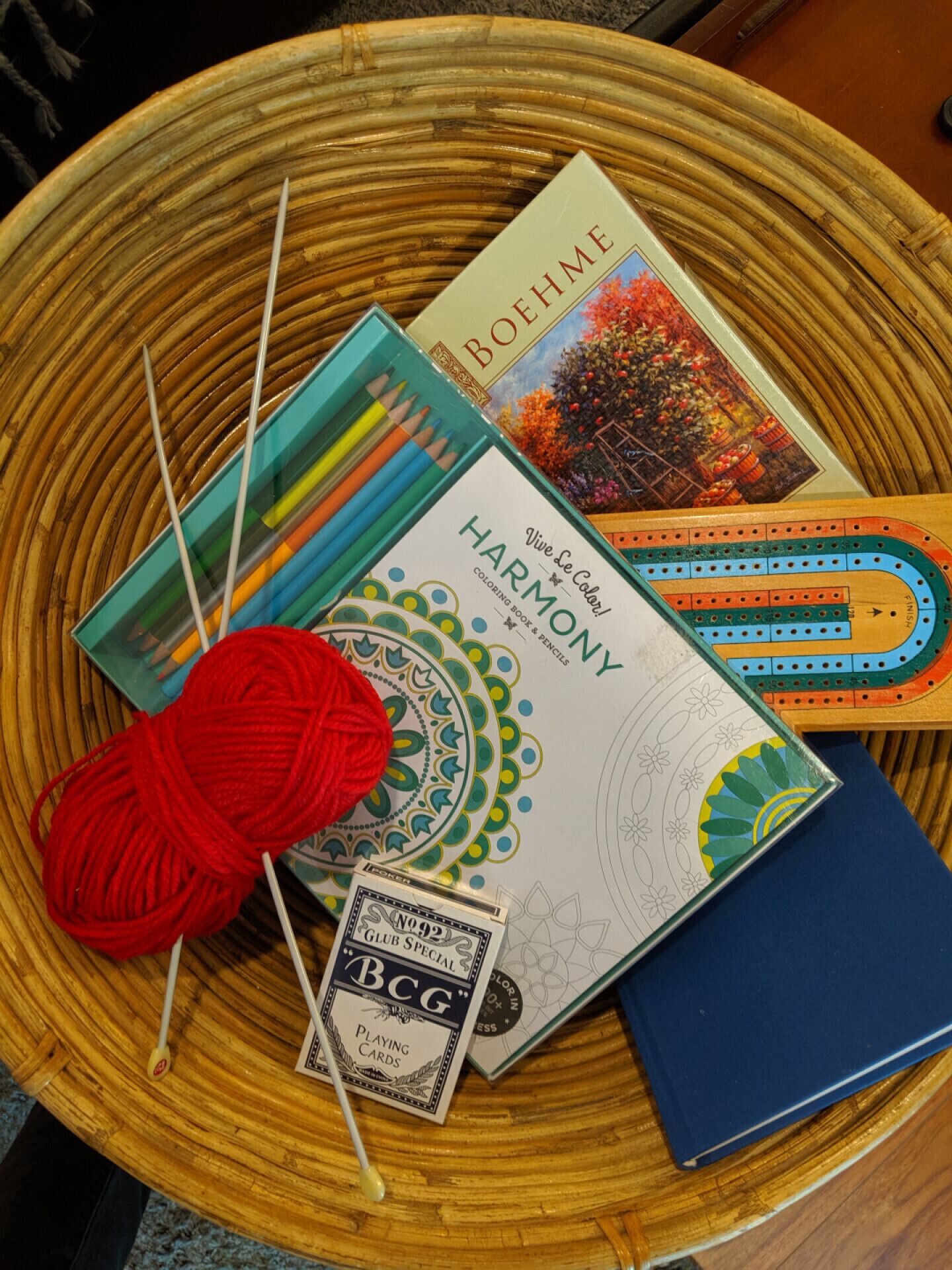 Una mesa con un libro titulado 'HARMONY', un juego de lápices de colores, un ovillo de lana roja, una cartulina de bingo y un juego de mesa de madera.