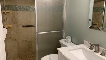 A bathroom with a glass-enclosed shower, a toilet, and a sink with a mirror above it.