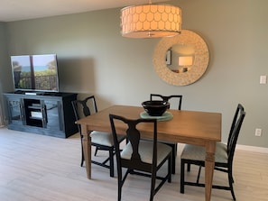 Un coin repas avec une table en bois, quatre chaises, un bol, une lampe et un téléviseur posé sur un meuble.