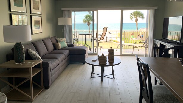 A living room with a sofa, a coffee table, and a TV. There is a balcony with a view of the ocean. - End of summer sale  Take a peek awesome reviews 50 feet from  sand (Longboat Key)