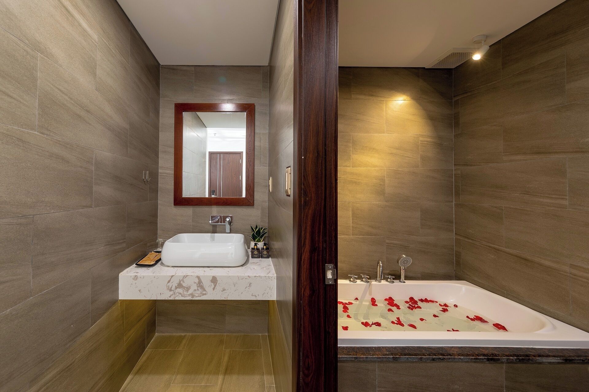 Un baño con lavabo, espejo y bañera con pétalos de rosa.