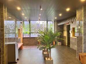 A modern lobby with a reception desk, potted plants, and a view of greenery outside. - Kiwi Beachside Hotel & Cafe Da Nang (Da Nang)