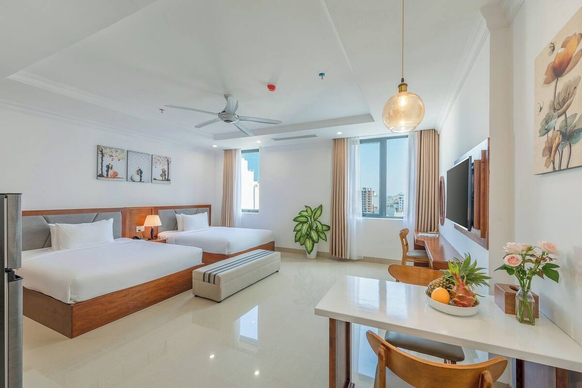 A hotel room with two beds, a dining table, a TV, and a ceiling fan.