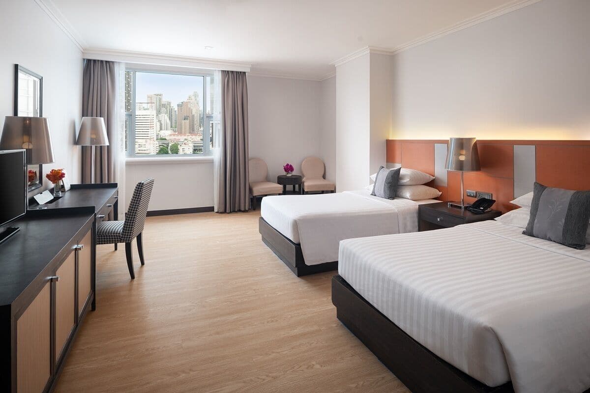A hotel room with two beds, a desk, a chair, a TV, and a window with a city view.