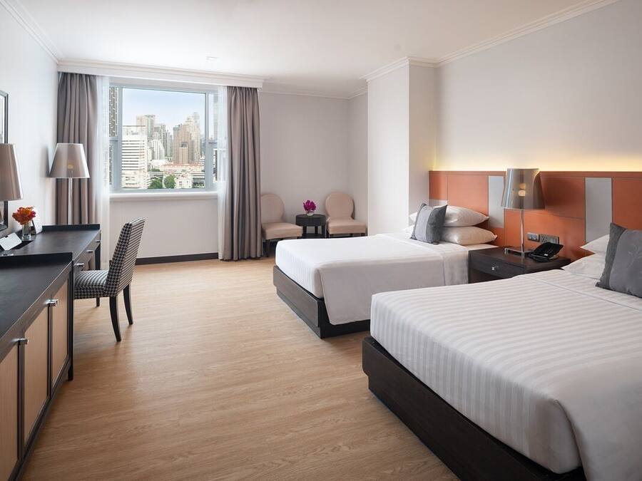 Habitación de hotel con dos camas, un escritorio, una silla, un televisor y una ventana con vistas a la ciudad.