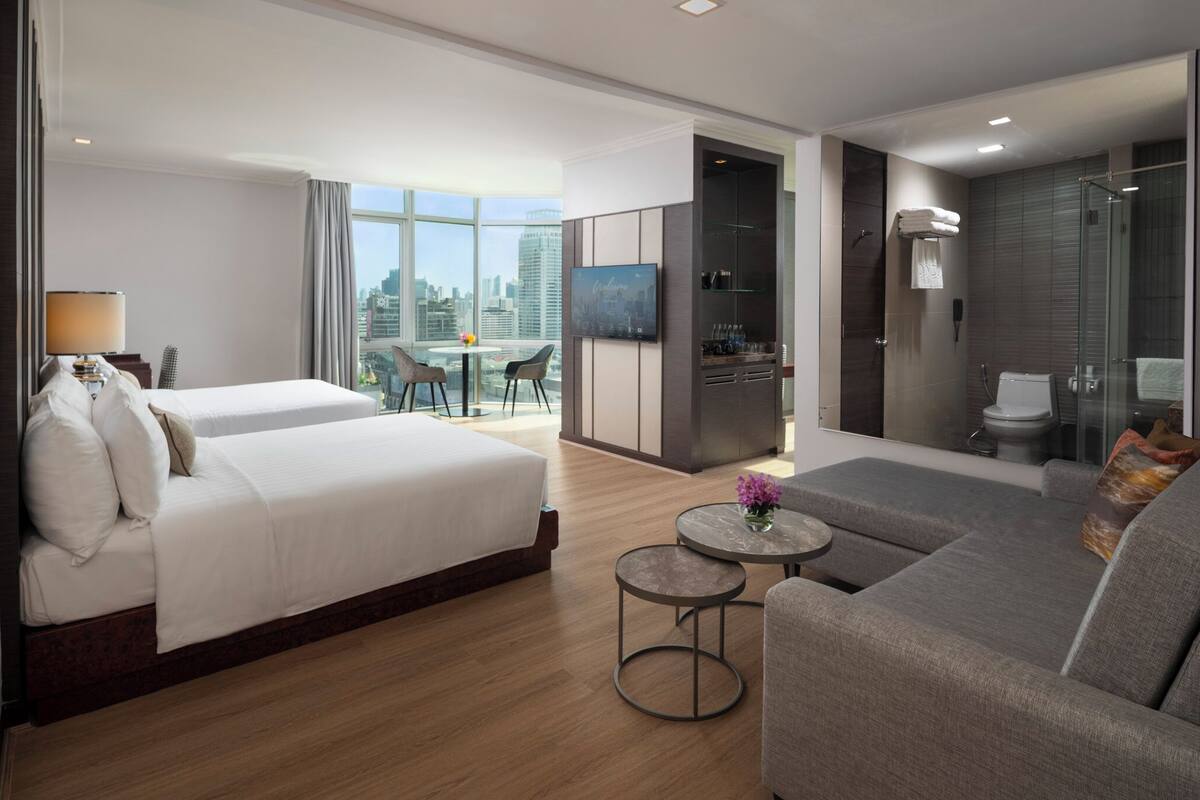 A modern hotel room with a large bed, a sofa, a small table, and a city view.