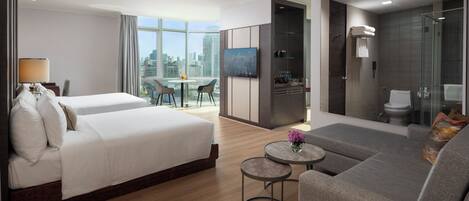 A modern hotel room with a large bed, a sofa, a small table, and a city view.