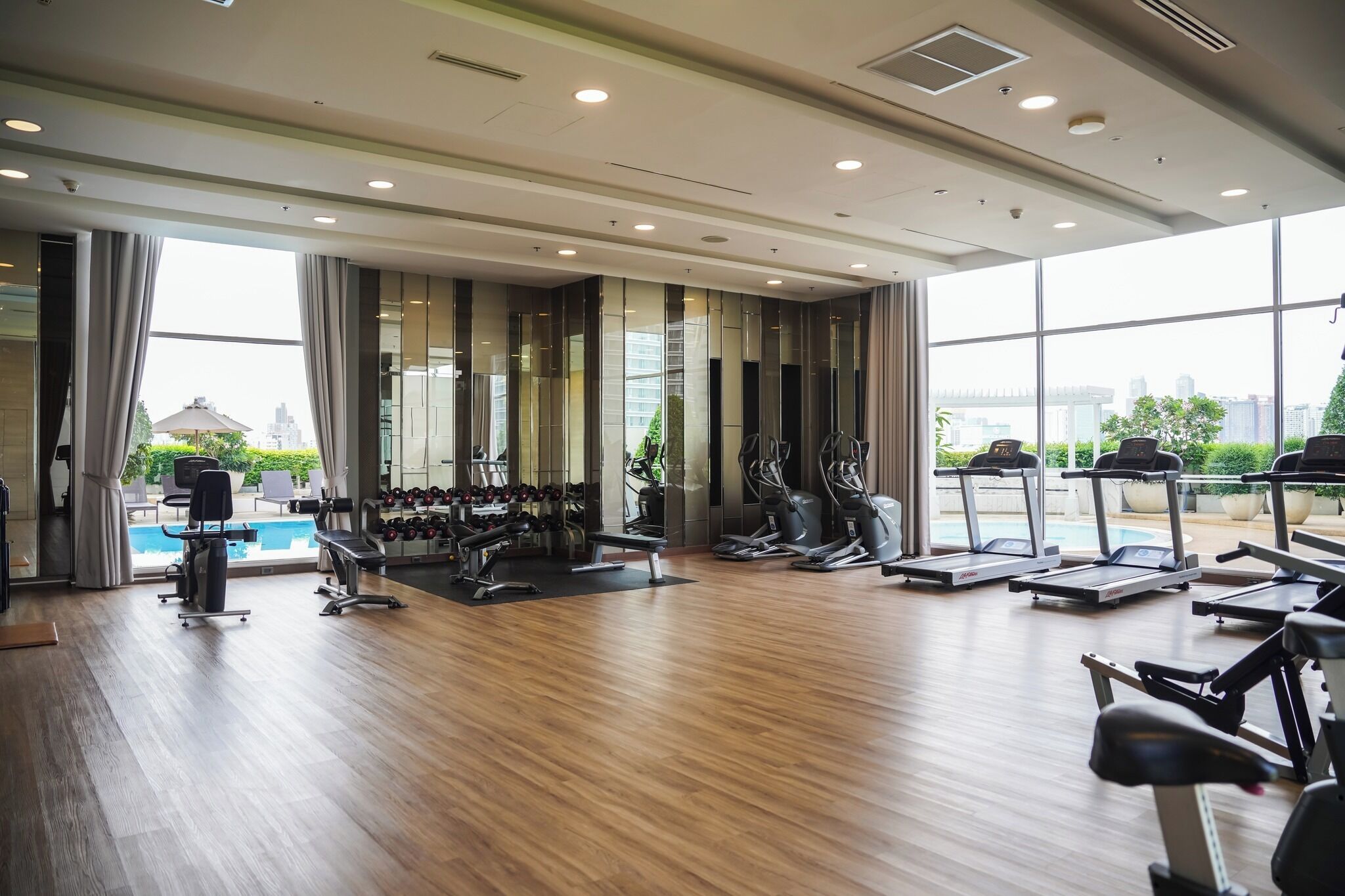 Ein Fitnessraum mit Trainingsgeräten, einem Pool und großen Fenstern mit Blick auf die Stadt.